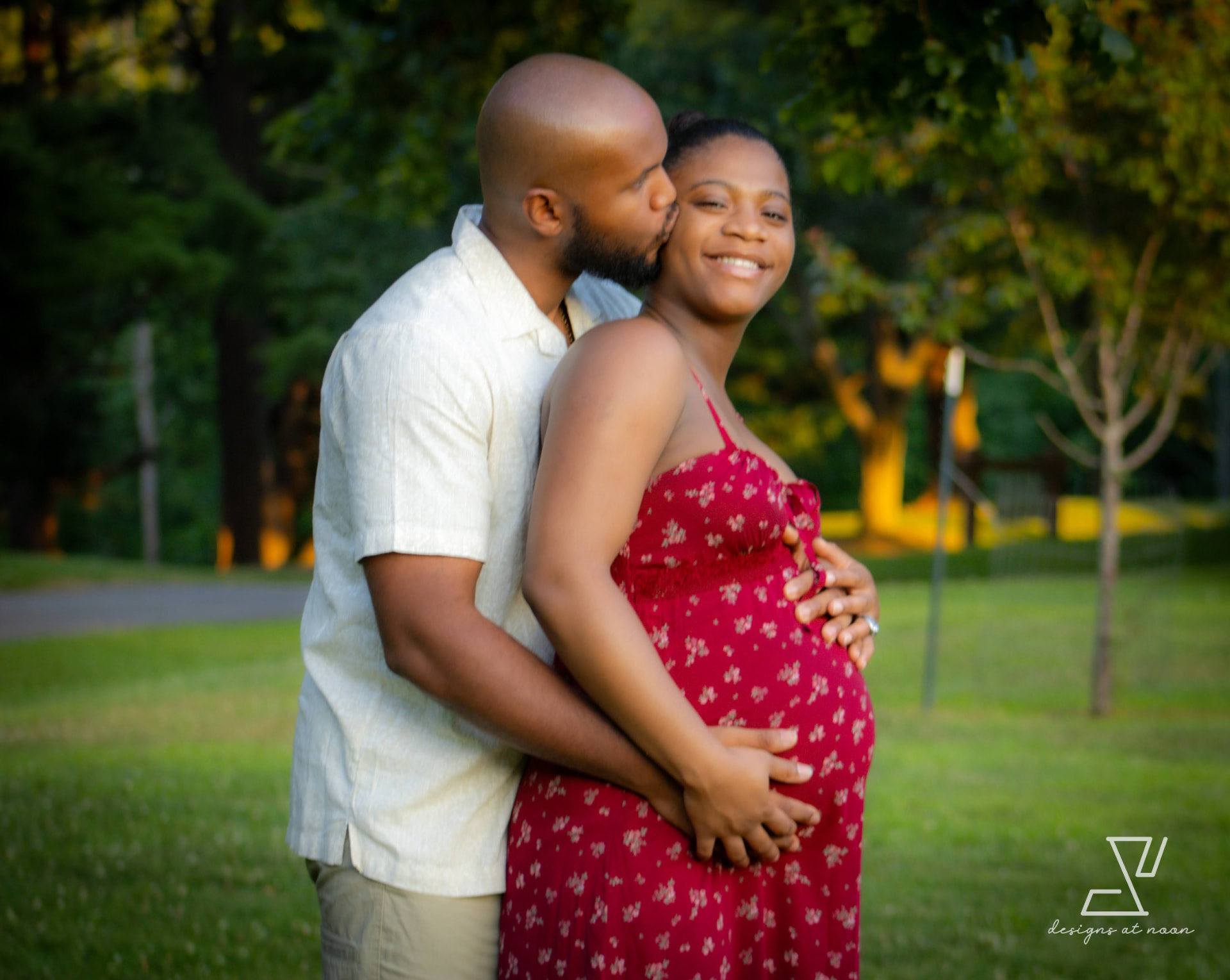 Expecting couple embracing in a park at sunset, hands resting on the bump