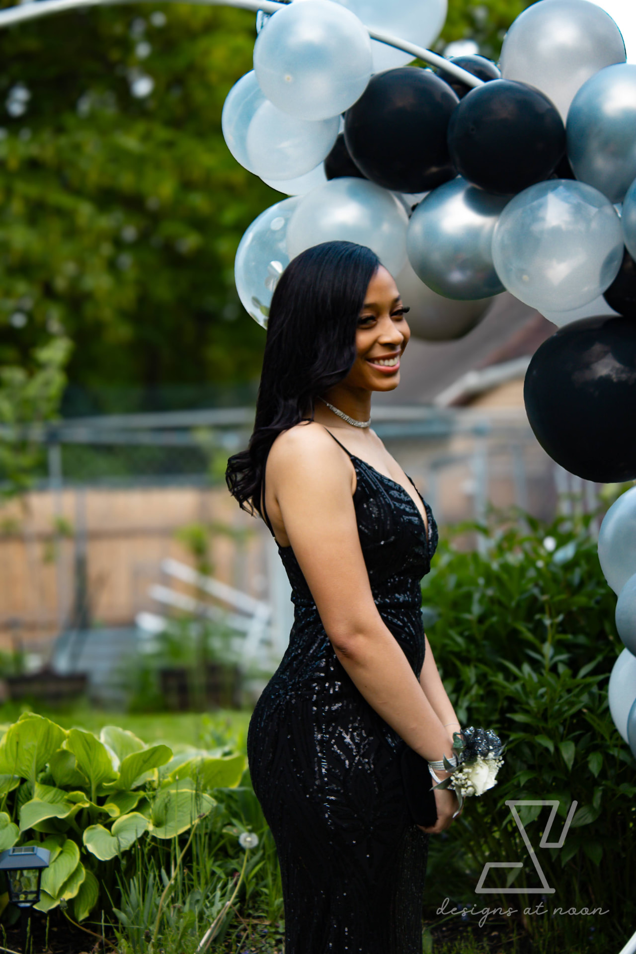 Prom portrait of a young woman in a black sequin gown among garden greenery