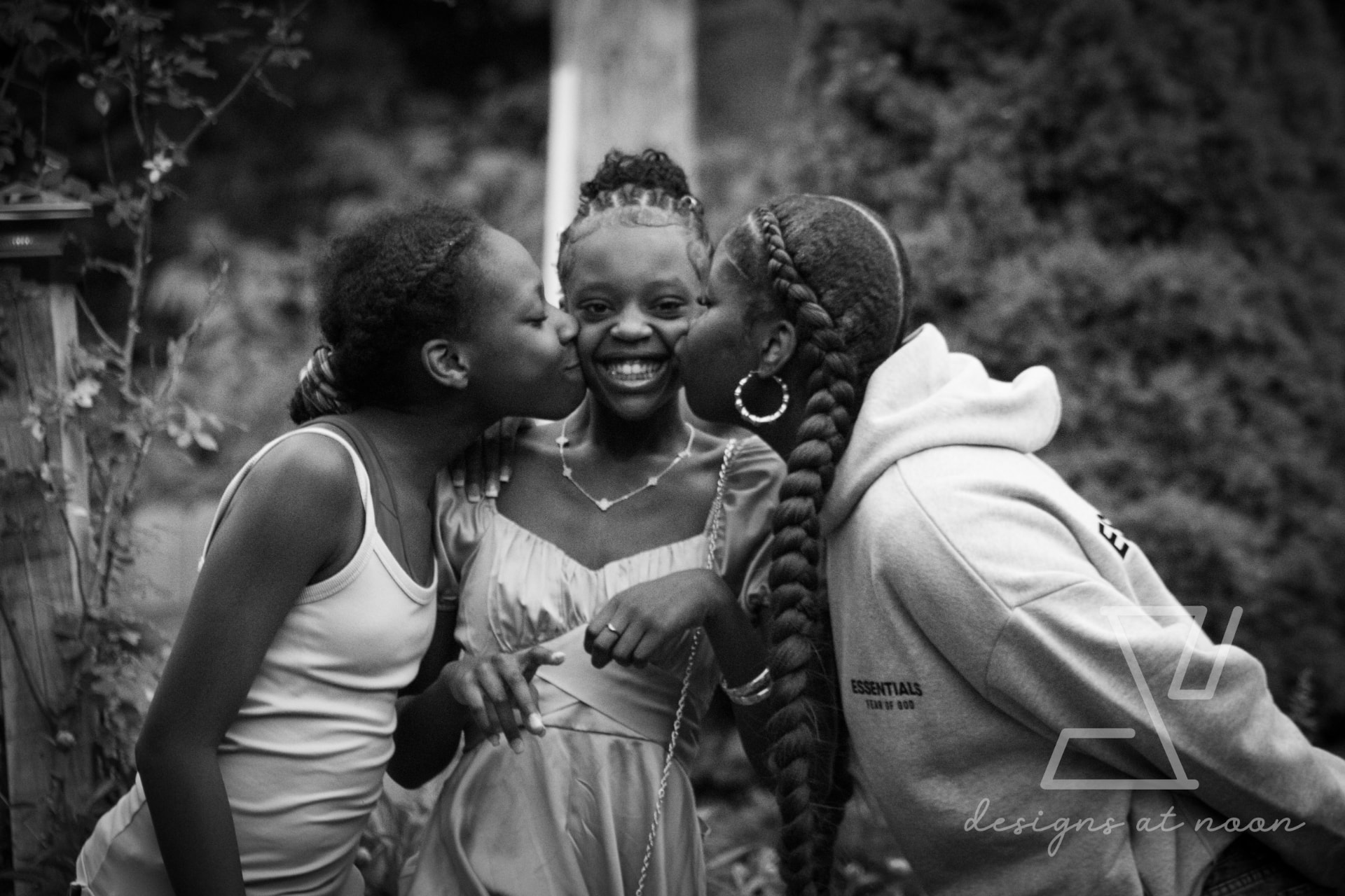 Black and white portrait of sisters kissing a smiling girl on both cheeks