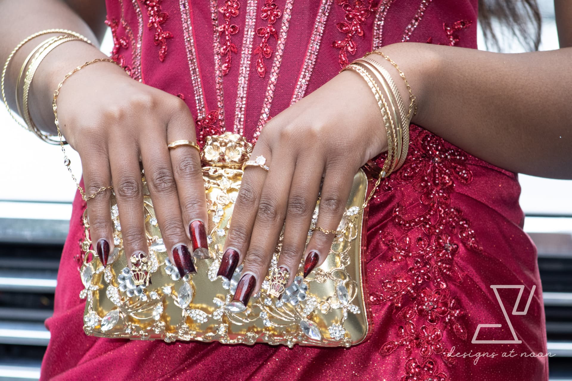 Detail of gold jeweled clutch, bangles and red nails against a red beaded gown