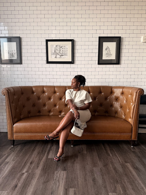 Shelanise Daniels, photographer, seated on a tan leather sofa in a white tiled studio space