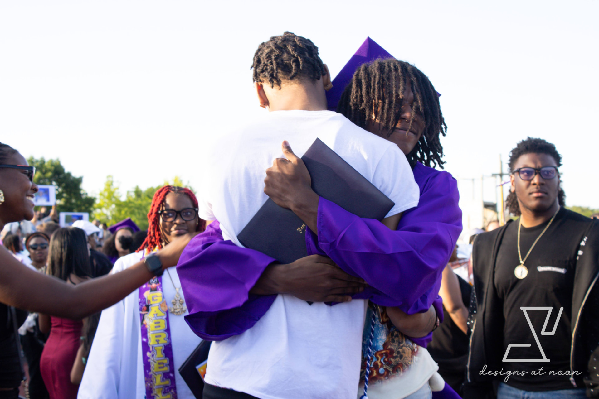 Graduate in a purple cap and gown embracing a friend after the ceremony