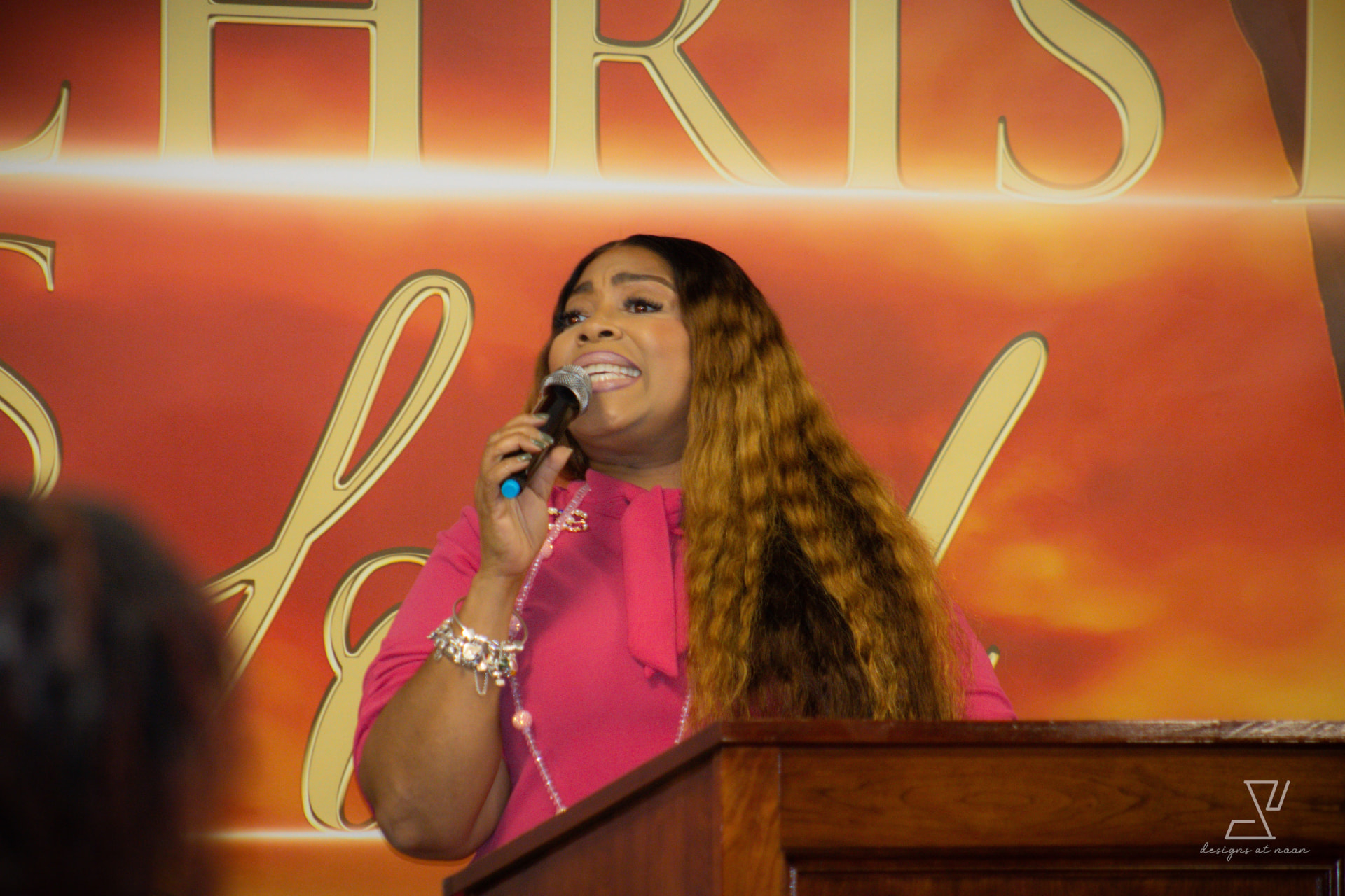 Woman in pink leading worship with a microphone at the pulpit